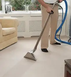 Professional carpet cleaner using a hot-water extraction wand and hose machine in a living room in Boston, MA.