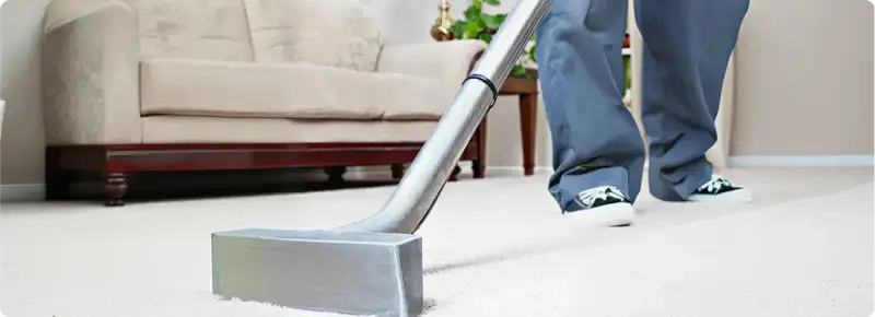 Carpet cleaning technician using a hot-water extraction wand on a light-colored carpet in a living room, Boston, MA.