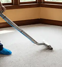 Steam carpet cleaning technician using a hot-water extraction wand on a residential carpet, wearing blue protective shoe covers Boston, MA.