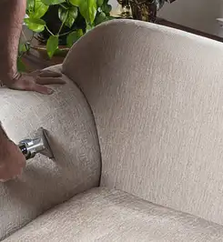 Professional upholstery cleaner deep-cleaning a fabric sofa with a handheld extraction tool and hose Boston, MA.