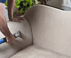 Professional upholstery cleaner deep-cleaning a fabric sofa with a handheld extraction tool and hose in Boston, MA.